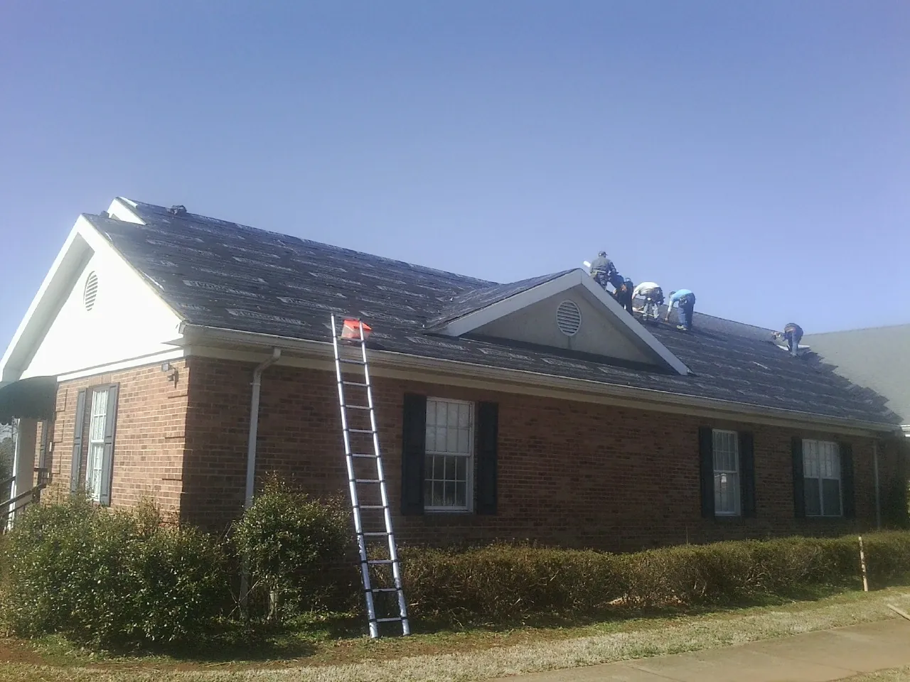 Crew tearing shingles off a brick ranch roof with a ladder set — Emergency Roof Repair work by our crew in Denmark